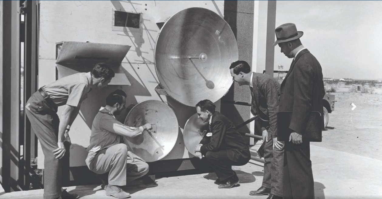 An old black and white photo showing engineers adjusting a satellite dish